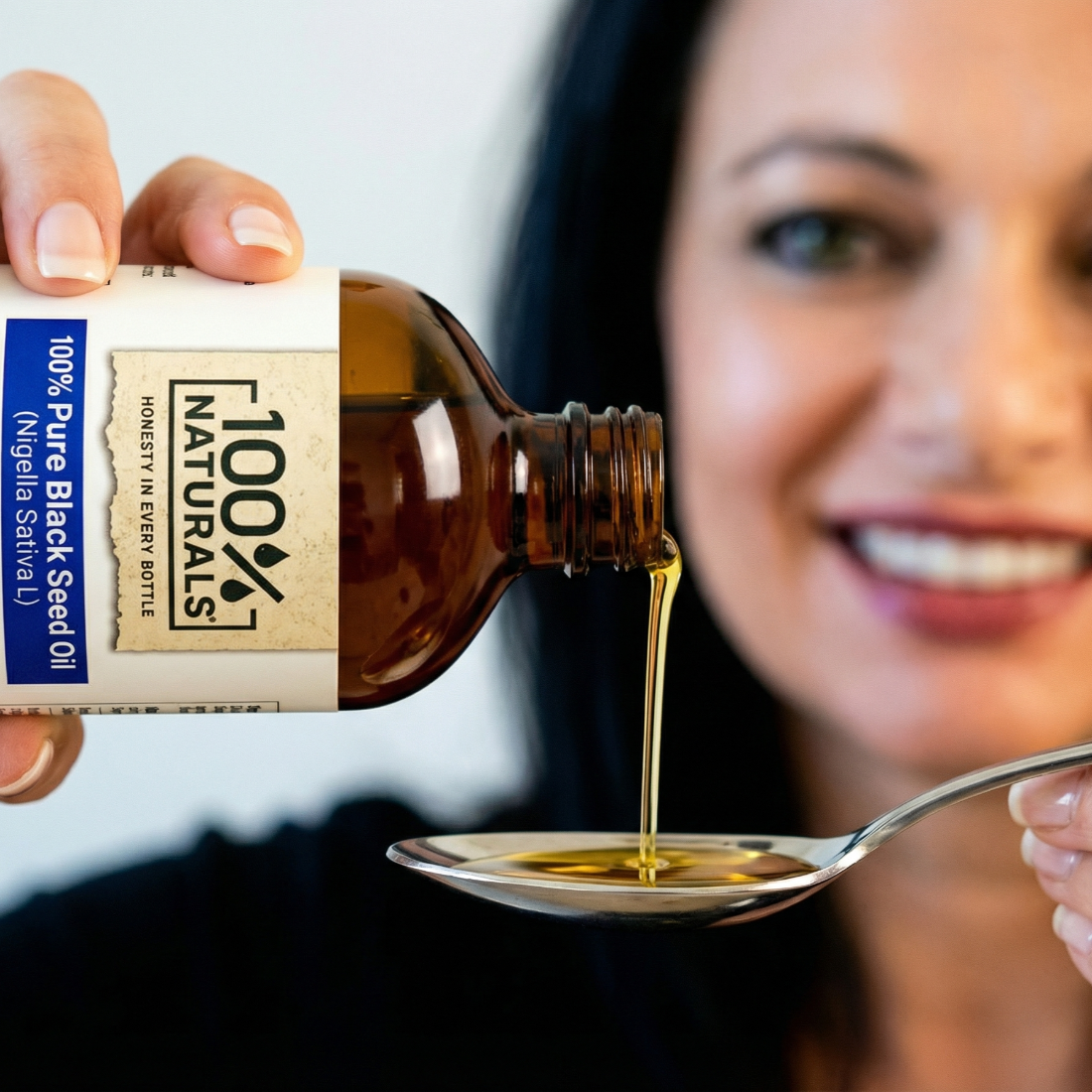 Bottle of 100 Naturals Black Seed Oil being poured onto a spoon.